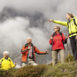 young female hiking guide showing senior group surrounding mountains, shallow focus, focus on young woman